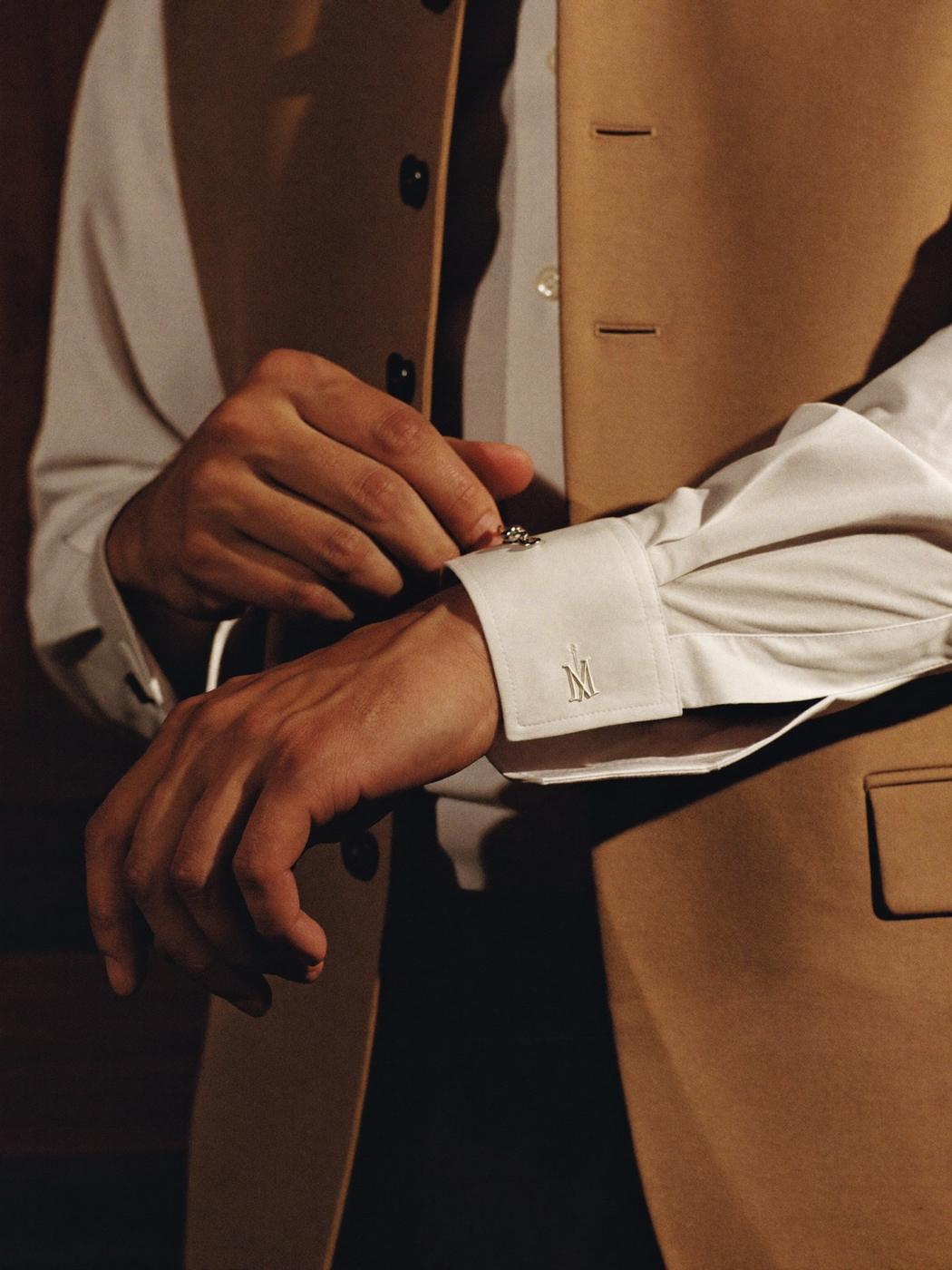 Close view of a man fastening the monogrammed cuff of a white bespoke shirt