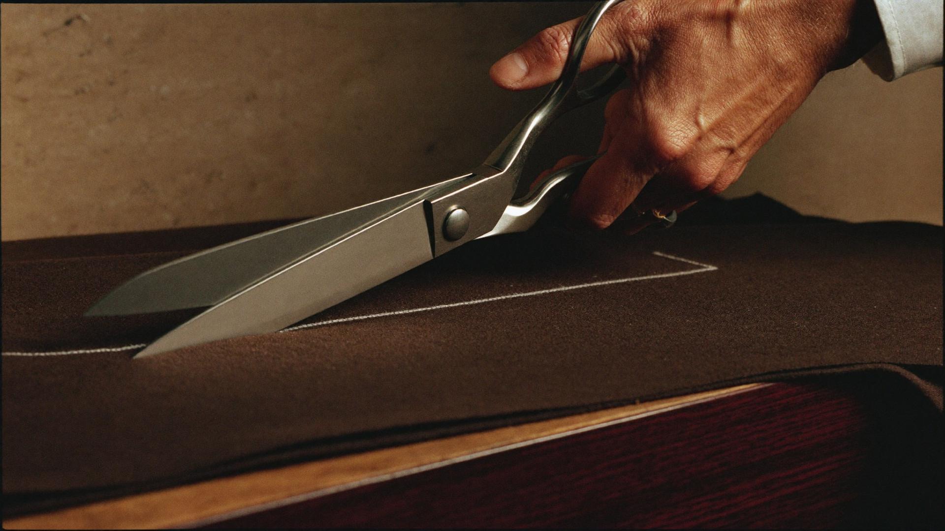 Tailor's shears cutting along chalk lines in brown wool fabric